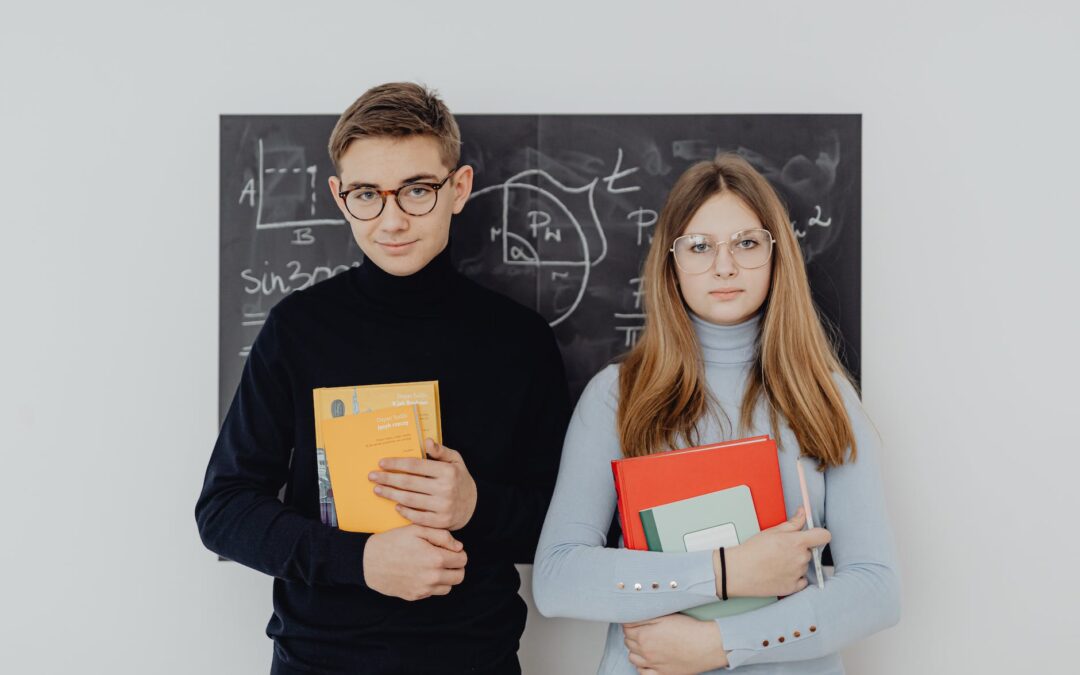 two teenagers with books against a blackboard