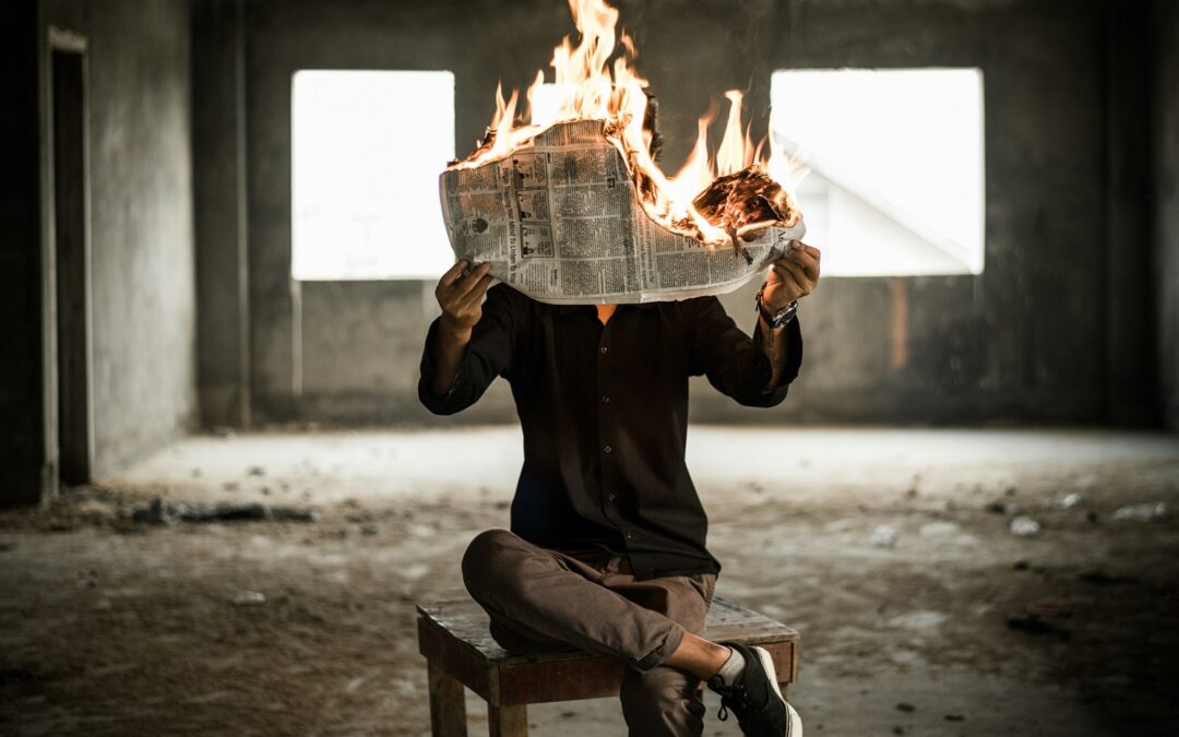 person sitting in an empty building holding a burning newspaper in their hands
