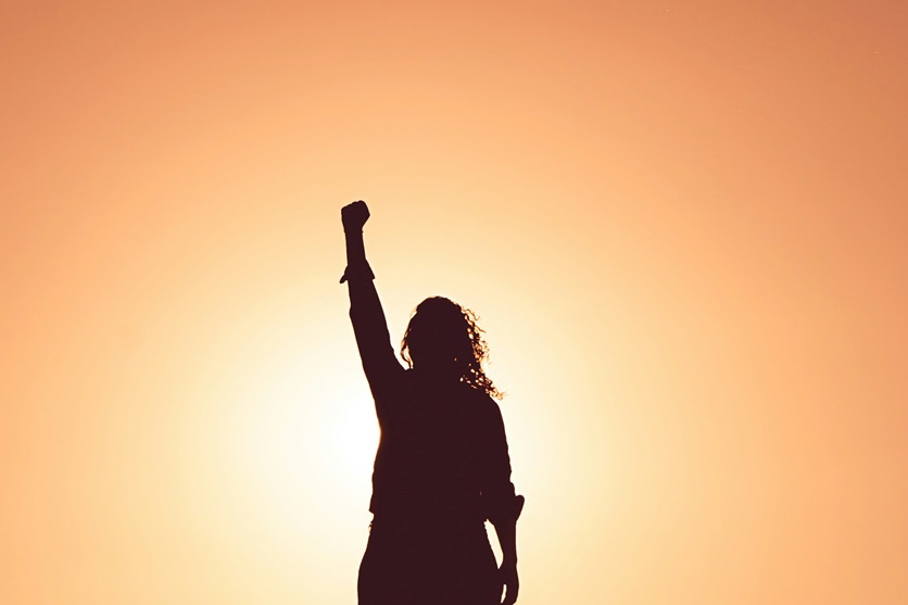 Woman raising her fist in the air in front of orange background