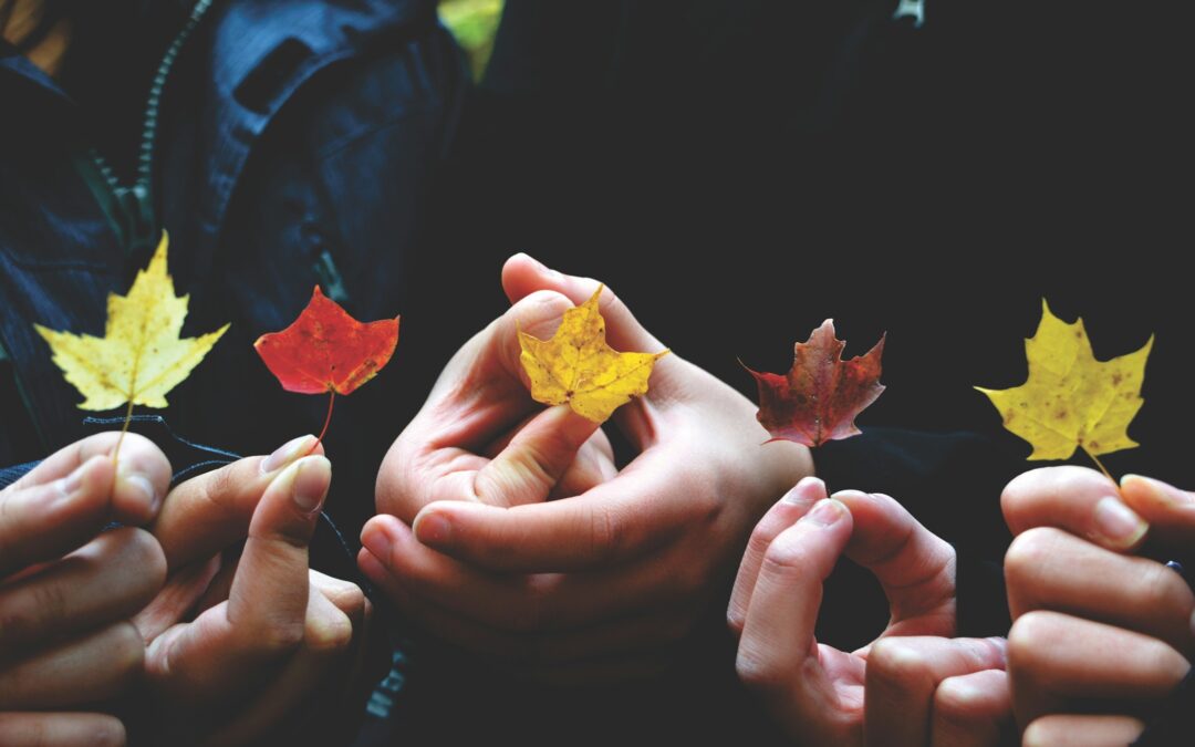 Five hands in a row holding autumn leaves