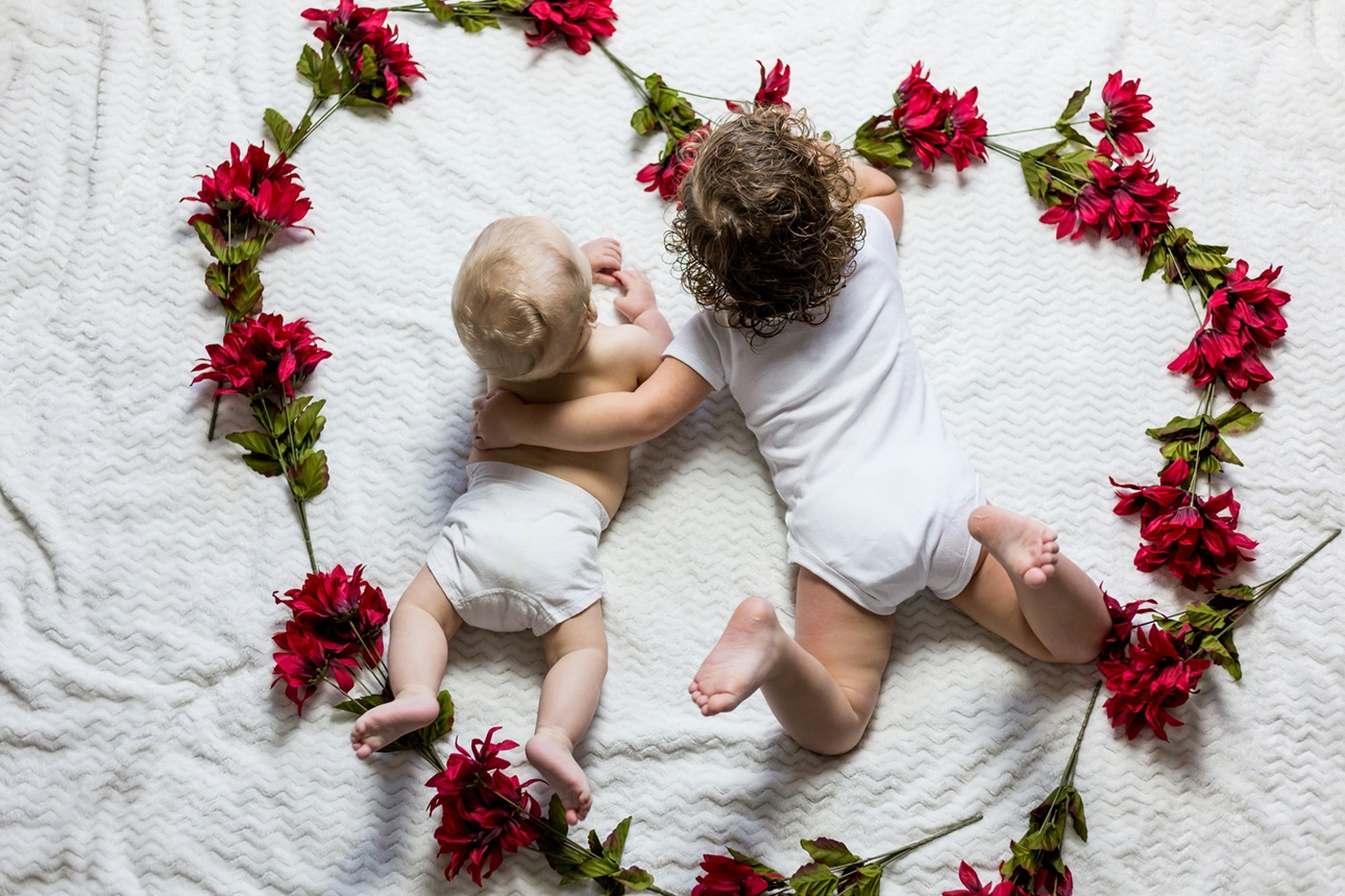 Baby and toddler lying side by side inside heart made of flowers