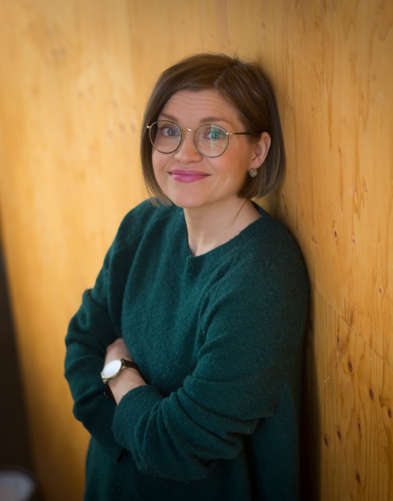 Portrait of smiling white woman with round glasses, chin-length mid-brown hair, and dark green knitted sweater.